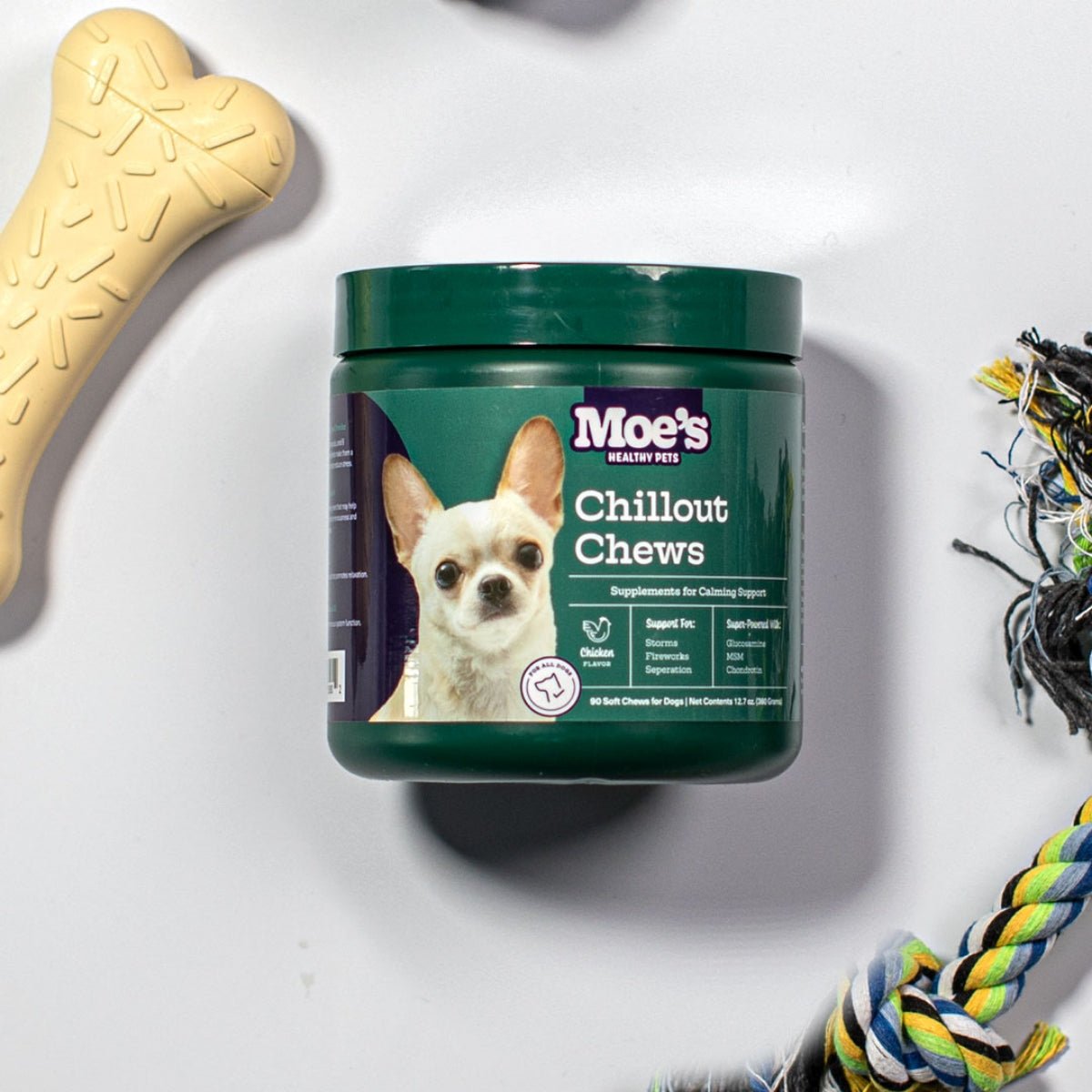 Container of Moe's Chillout Chews for dogs with a dog toy and rope on a white background