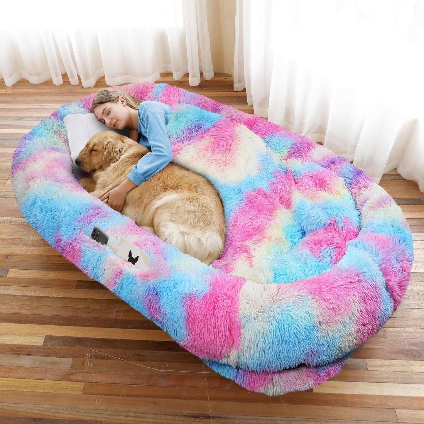 Woman lying on a colorful donut-shaped pet bed with a dog, in a room with curtains.