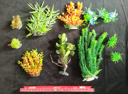 Assorted artificial aquarium plants on a black background with a ruler at the bottom.