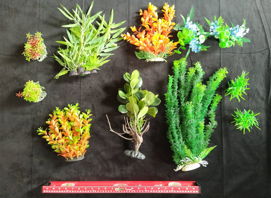 Assorted artificial aquarium plants on a black background with a ruler at the bottom.