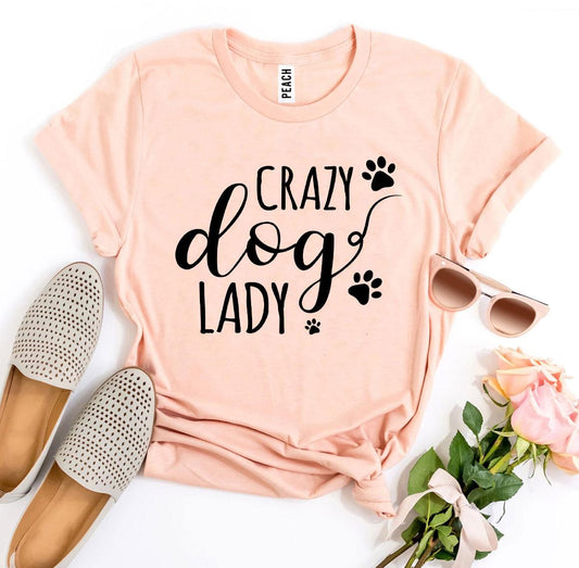 Pink t-shirt with 'Crazy Dog Lady' text, accompanied by flat shoes, sunglasses, and flowers on a white background.