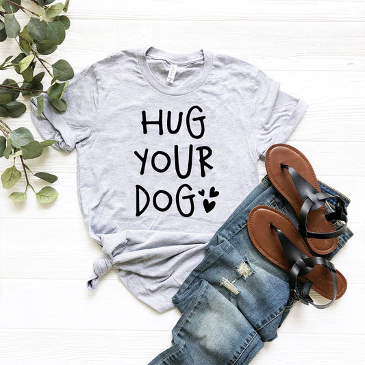 Gray t-shirt with 'HUG YOUR DOG' text, paired with jeans and sandals on a white background.