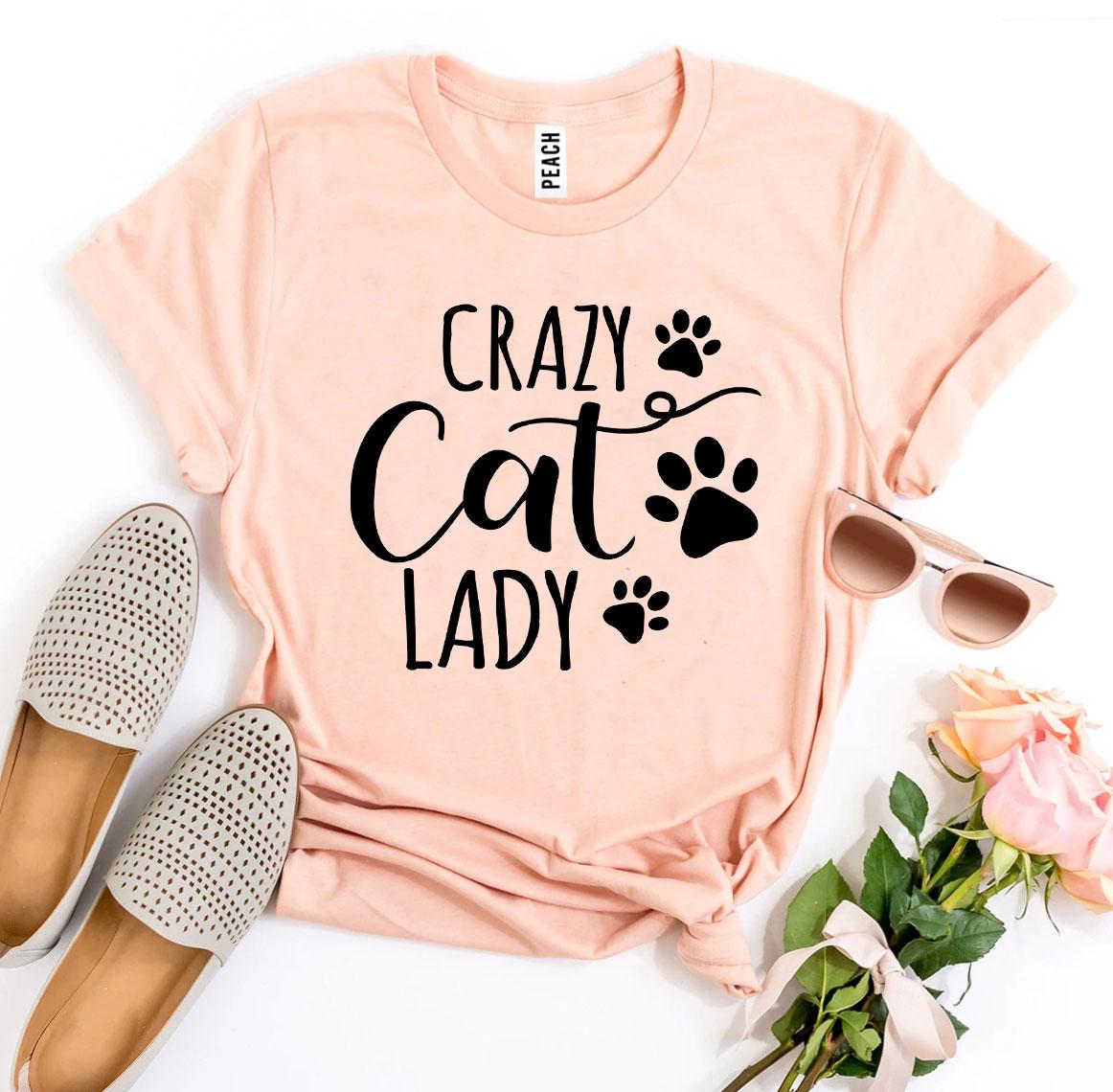 Peach t-shirt with 'Crazy Cat Lady' text and paw prints, paired with flats, sunglasses, and flowers on a white background.