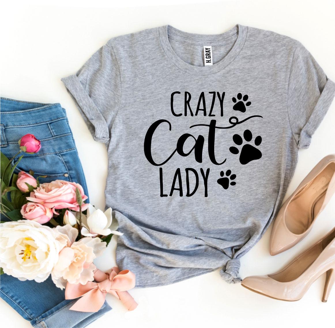 Gray t-shirt with 'Crazy Cat Lady' text and paw prints, paired with jeans, shoes, and flowers on a white background.