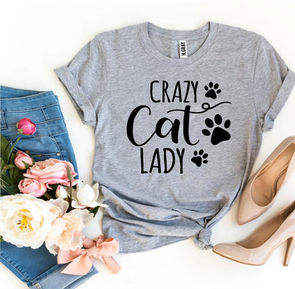 Gray t-shirt with 'Crazy Cat Lady' text and paw prints, paired with jeans, shoes, and flowers on a white background.