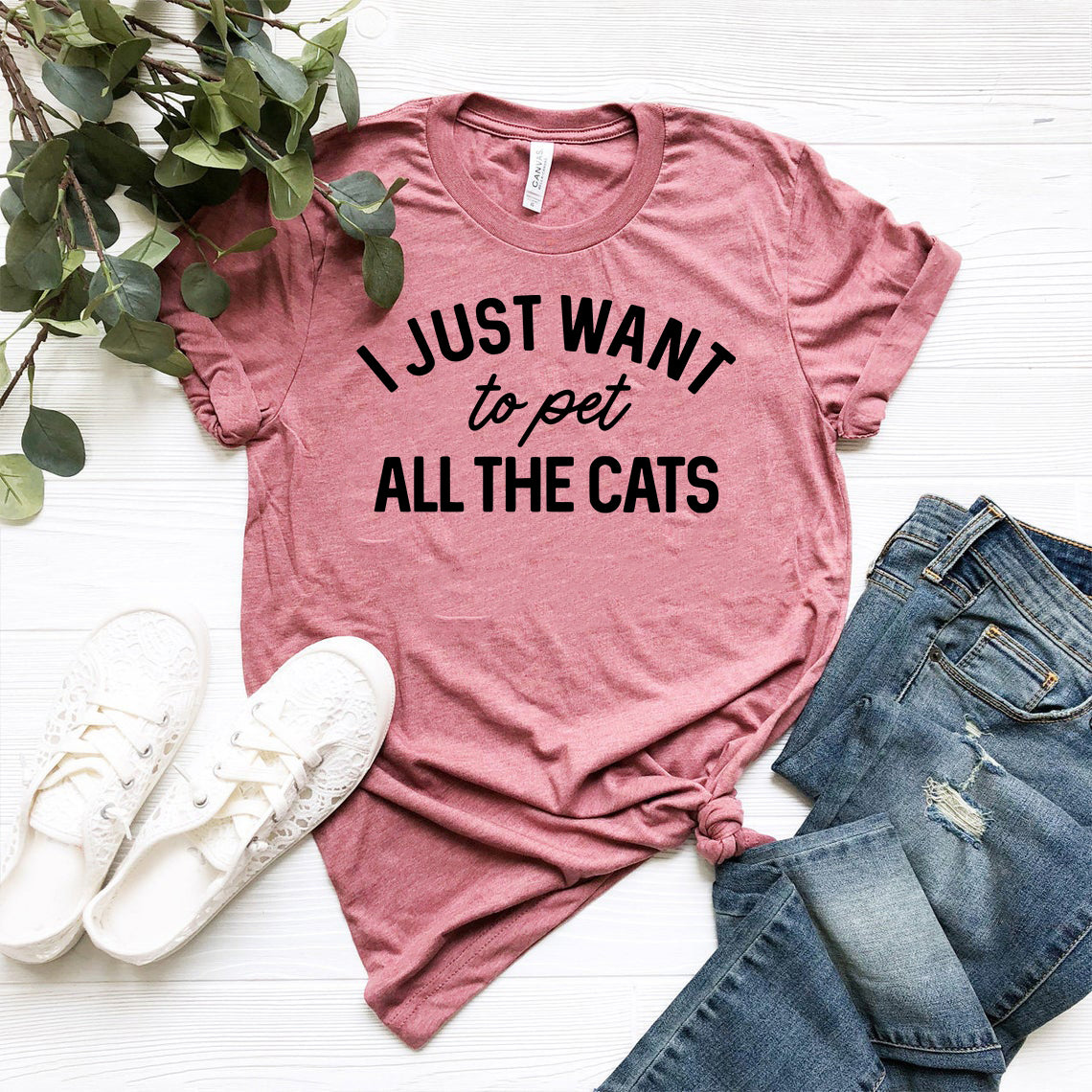 Pink t-shirt with 'I Just Want to Pet All the Cats' text, paired with jeans and sneakers on a white surface.