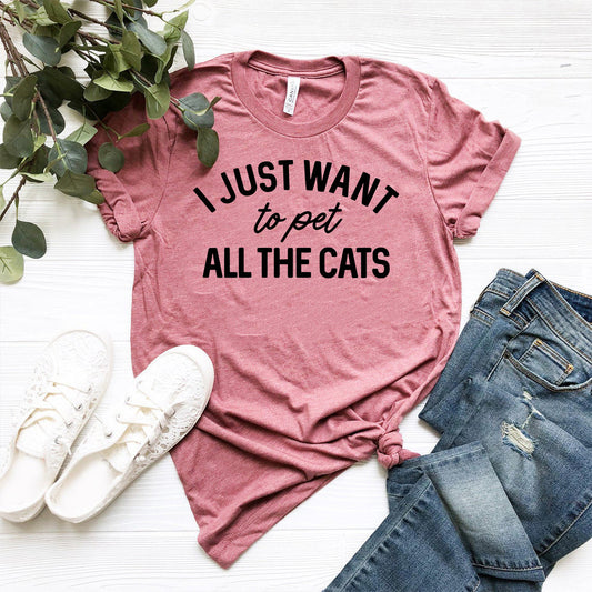 Pink t-shirt with 'I Just Want to Pet All the Cats' text, paired with jeans and sneakers on a white surface.