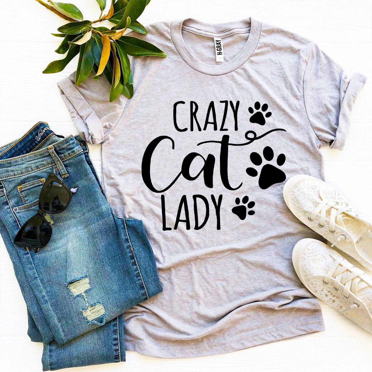 Gray t-shirt with 'Crazy Cat Lady' text and paw prints, paired with jeans and sneakers on a white background.