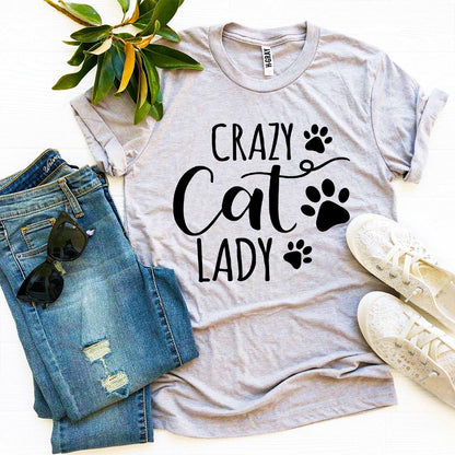 Gray t-shirt with 'Crazy Cat Lady' text and paw prints, paired with jeans and sneakers on a white background.