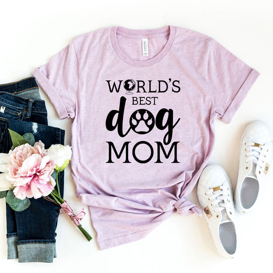 Pink t-shirt with 'World's Best Dog Mom' text, jeans, sneakers, and flowers on a white background