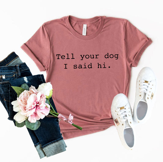 Pink t-shirt with 'Tell your dog I said hi.' text, jeans, sneakers, and flowers on a white background