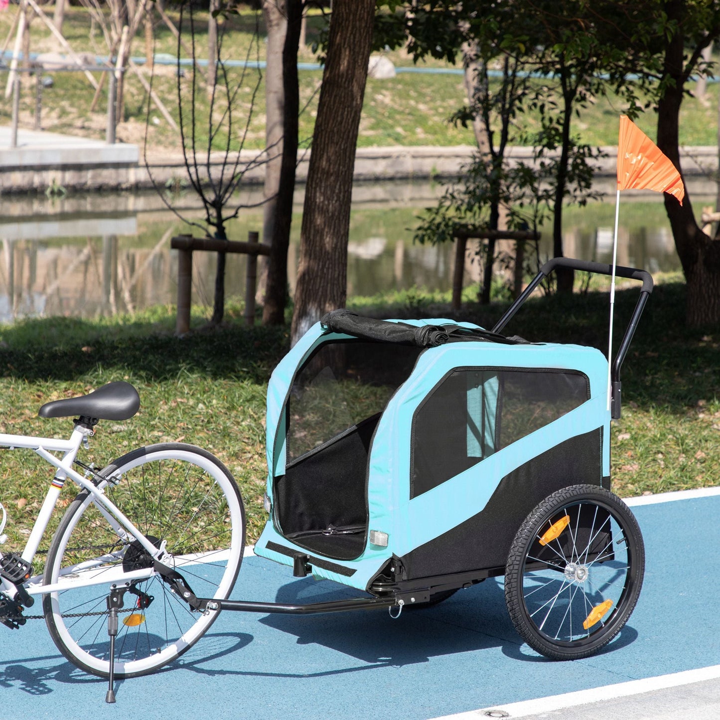 Bicycle with a blue and black trailer attached, parked on a path near a park.