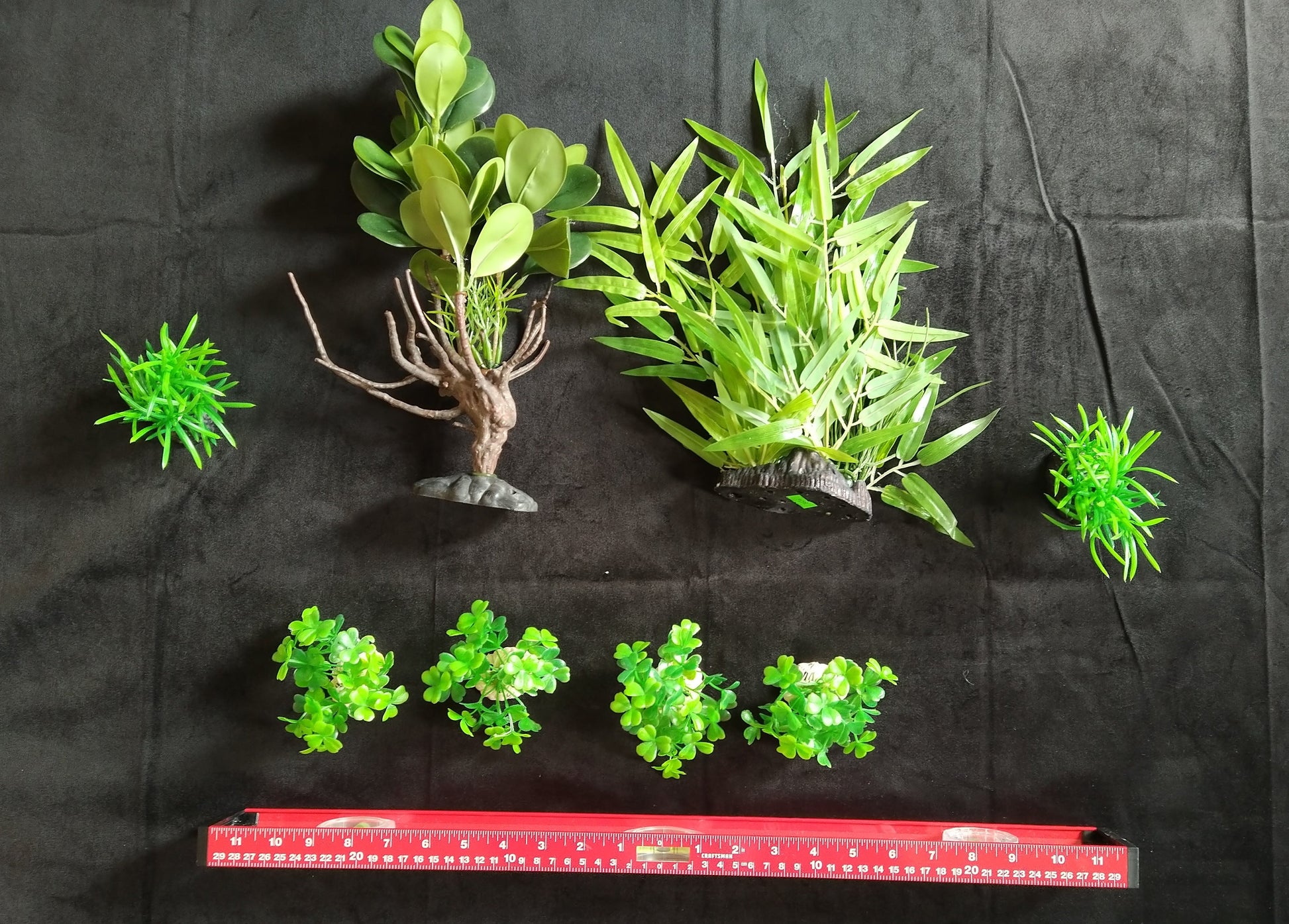 Set of green artificial plants on a black background with a red ruler for scale.