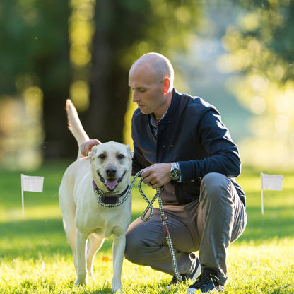 Man with a dog on a grassy field with trees in the background
