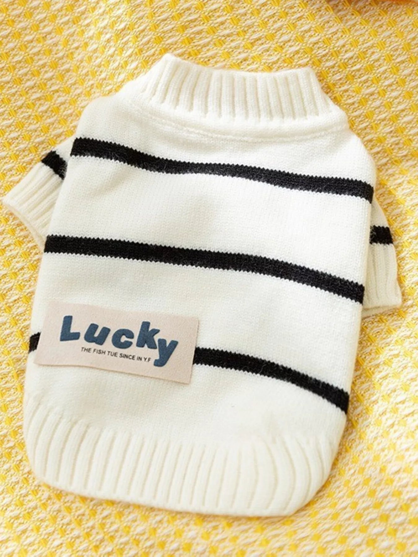 White sweater with black stripes and 'Lucky' tag on a yellow textured background