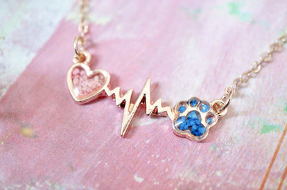 Necklace with heart, heartbeat line, and paw print charm on a pink background