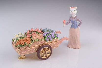 Cat figurine with a wheelbarrow full of flowers on a gray background
