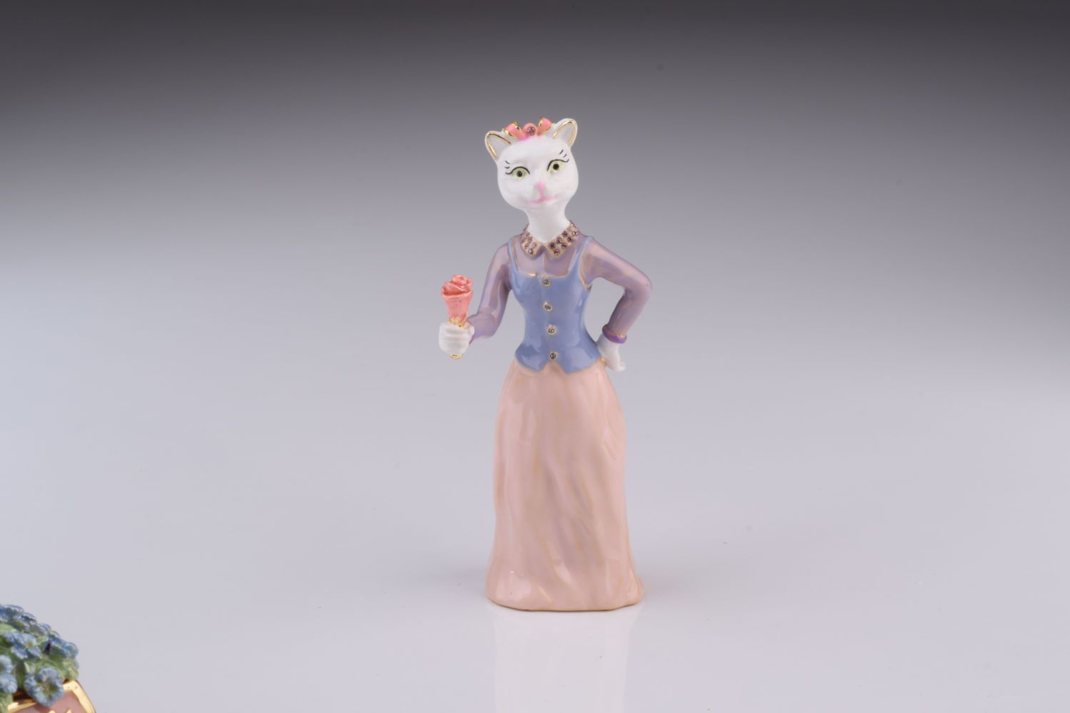 Cat figurine in a dress holding a flower on a gray background