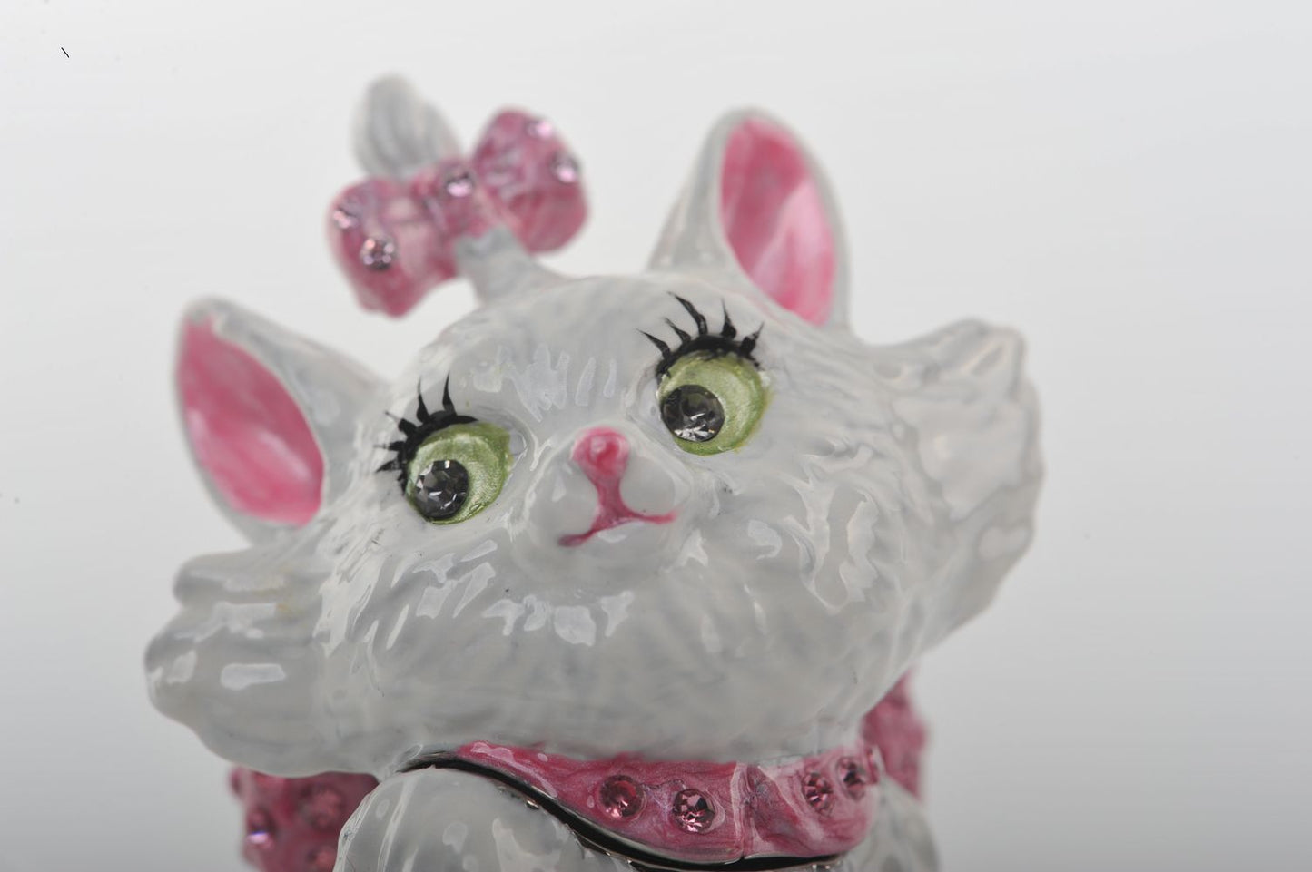 Decorative cat figurine with pink bow and green eyes on a white background