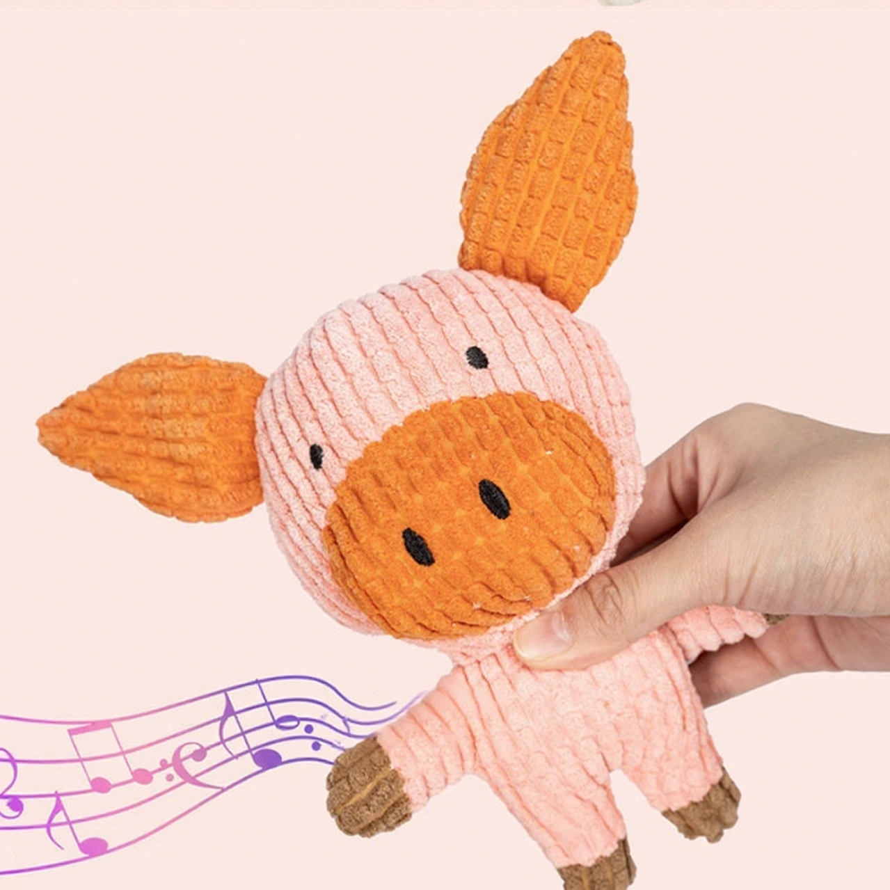Hand holding a small plush toy with orange ears and face on a light pink background