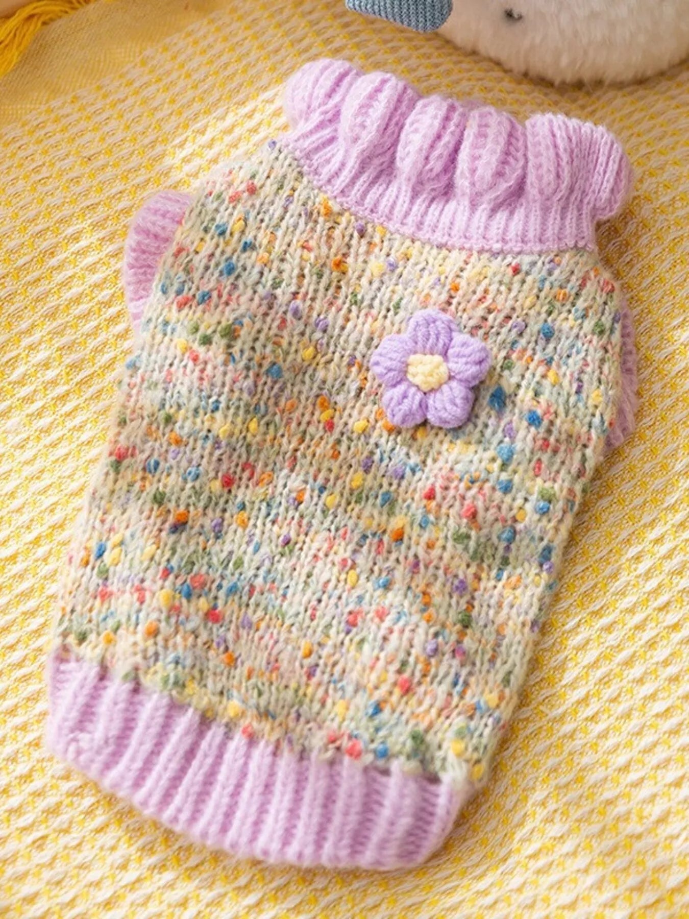 Knitted pet sweater with colorful pattern and pink trim on a yellow textured background
