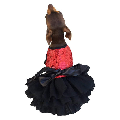 Small dog wearing a red sequin dress with a black ruffled skirt on a white background