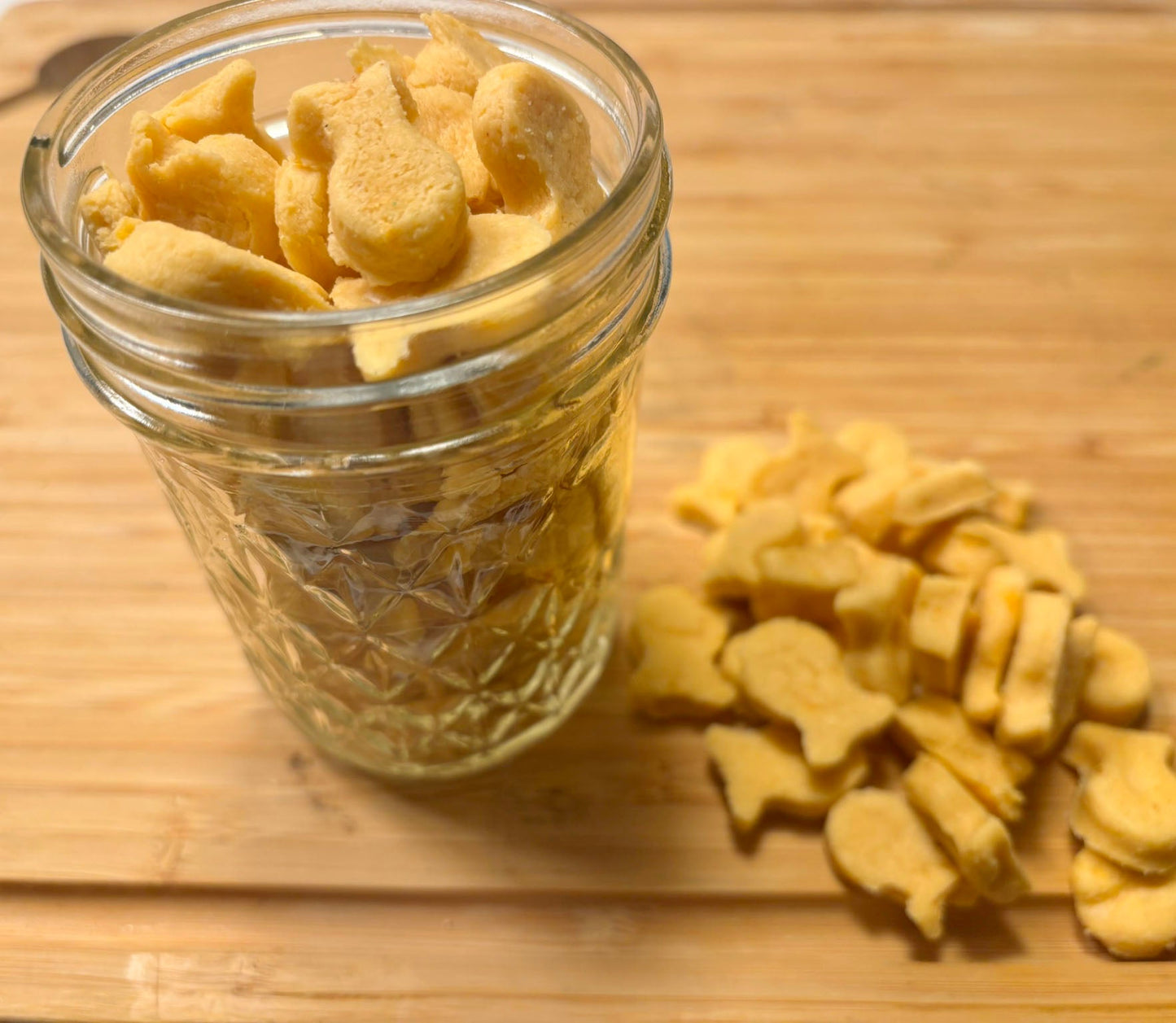 Glass jar filled with dog treats shaped like bones on a wooden surface.