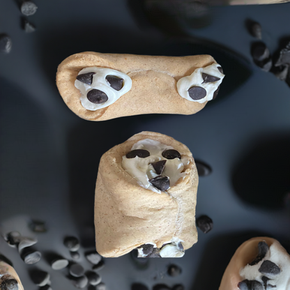 Two cookie-shaped treats with chocolate chip eyes on a dark surface.