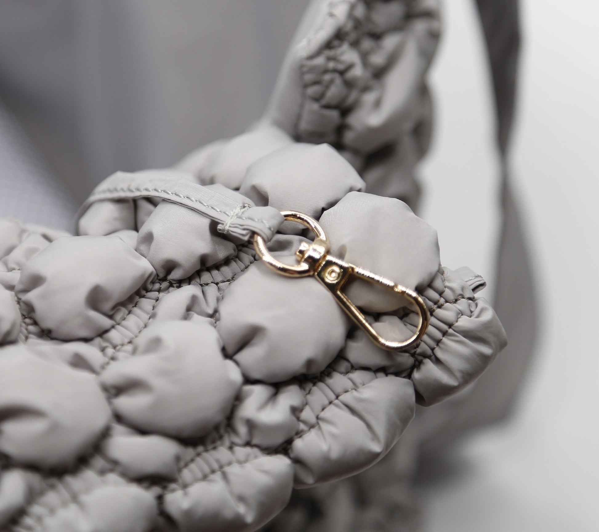 Close-up of a textured gray bag with a gold clasp on a neutral background
