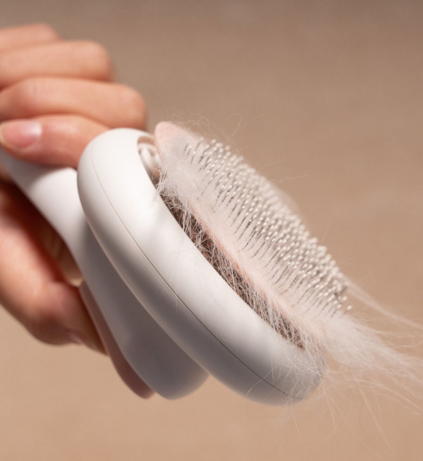 Person using a hair removal brush with hair collected on it against a beige background