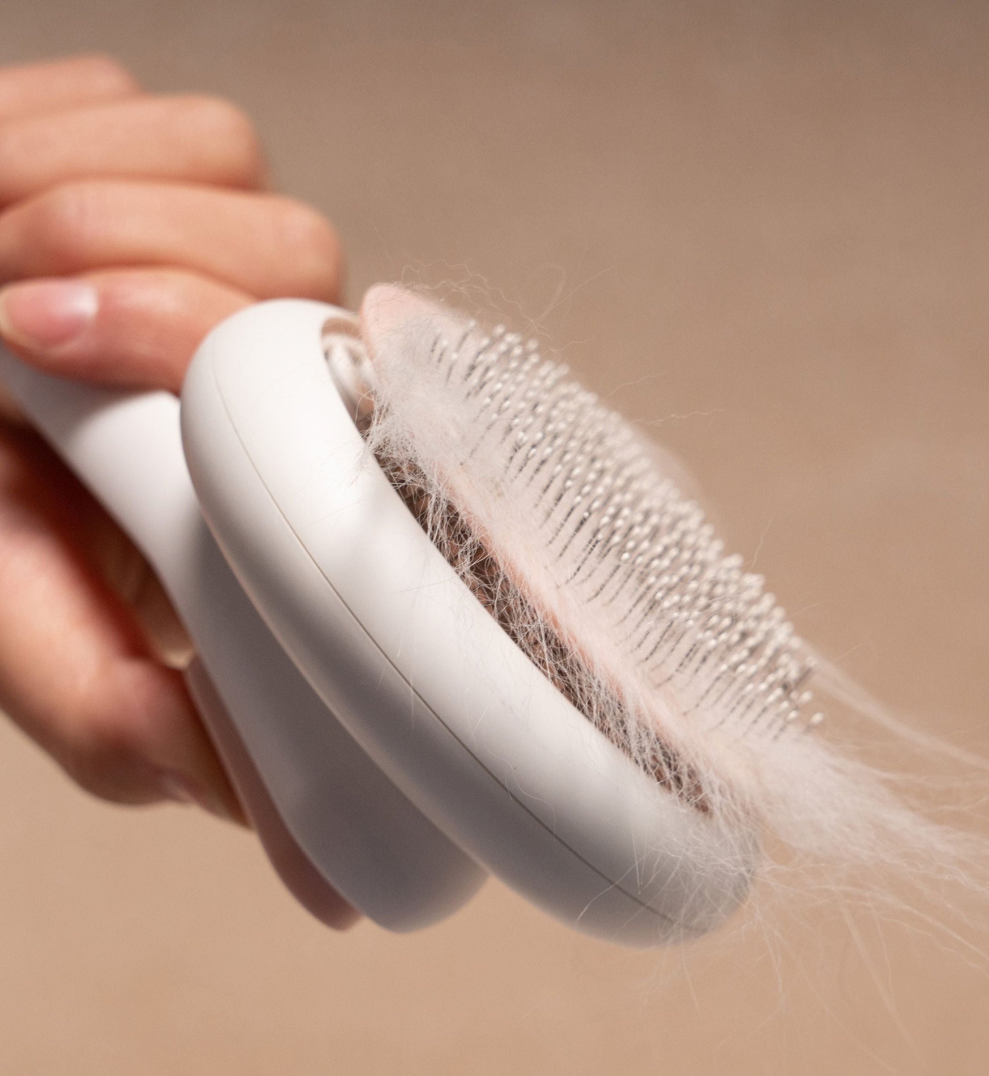Person using a hair removal brush with hair collected on it against a beige background