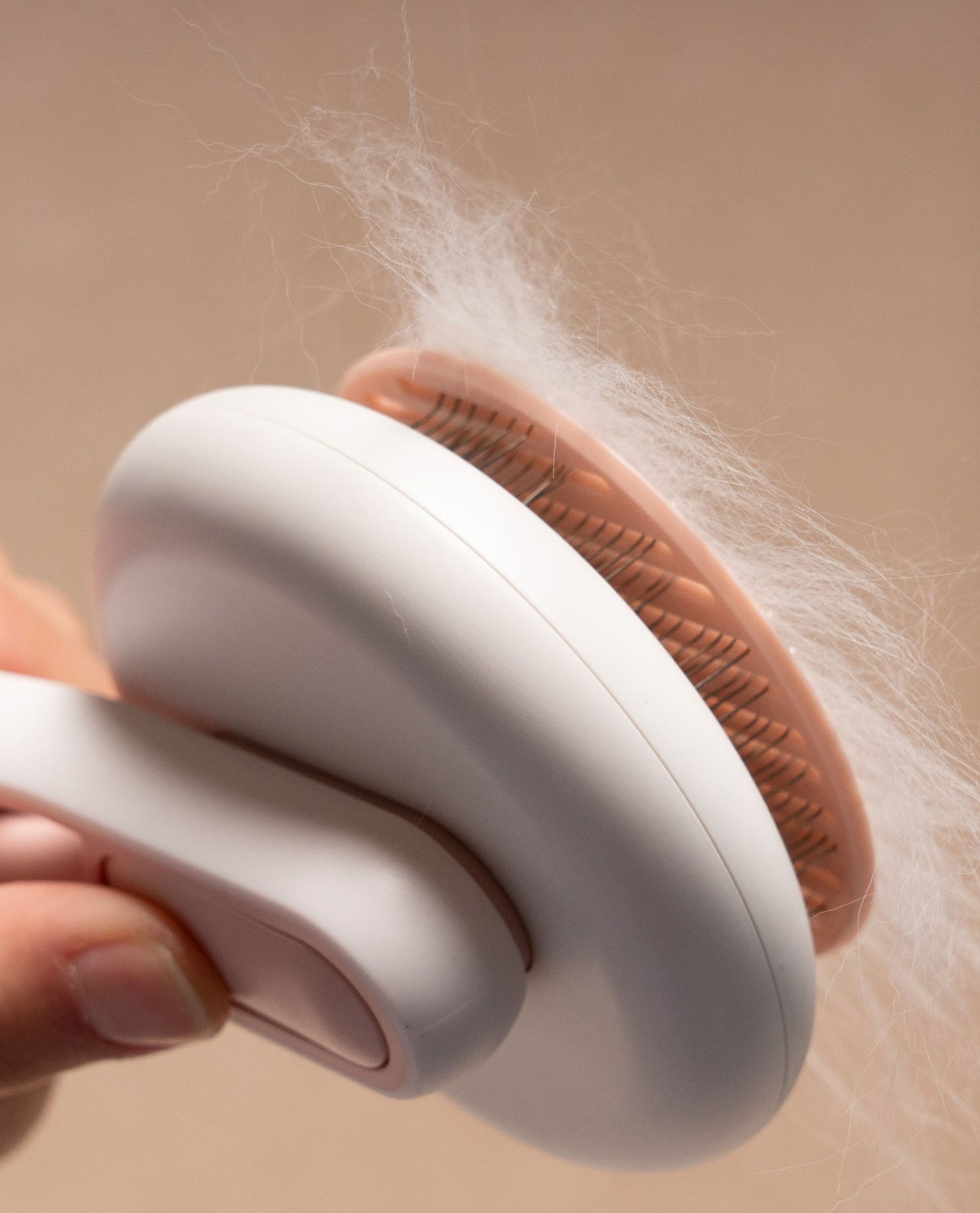 Person using a white grooming brush with pink bristles to remove hair from a beige surface.
