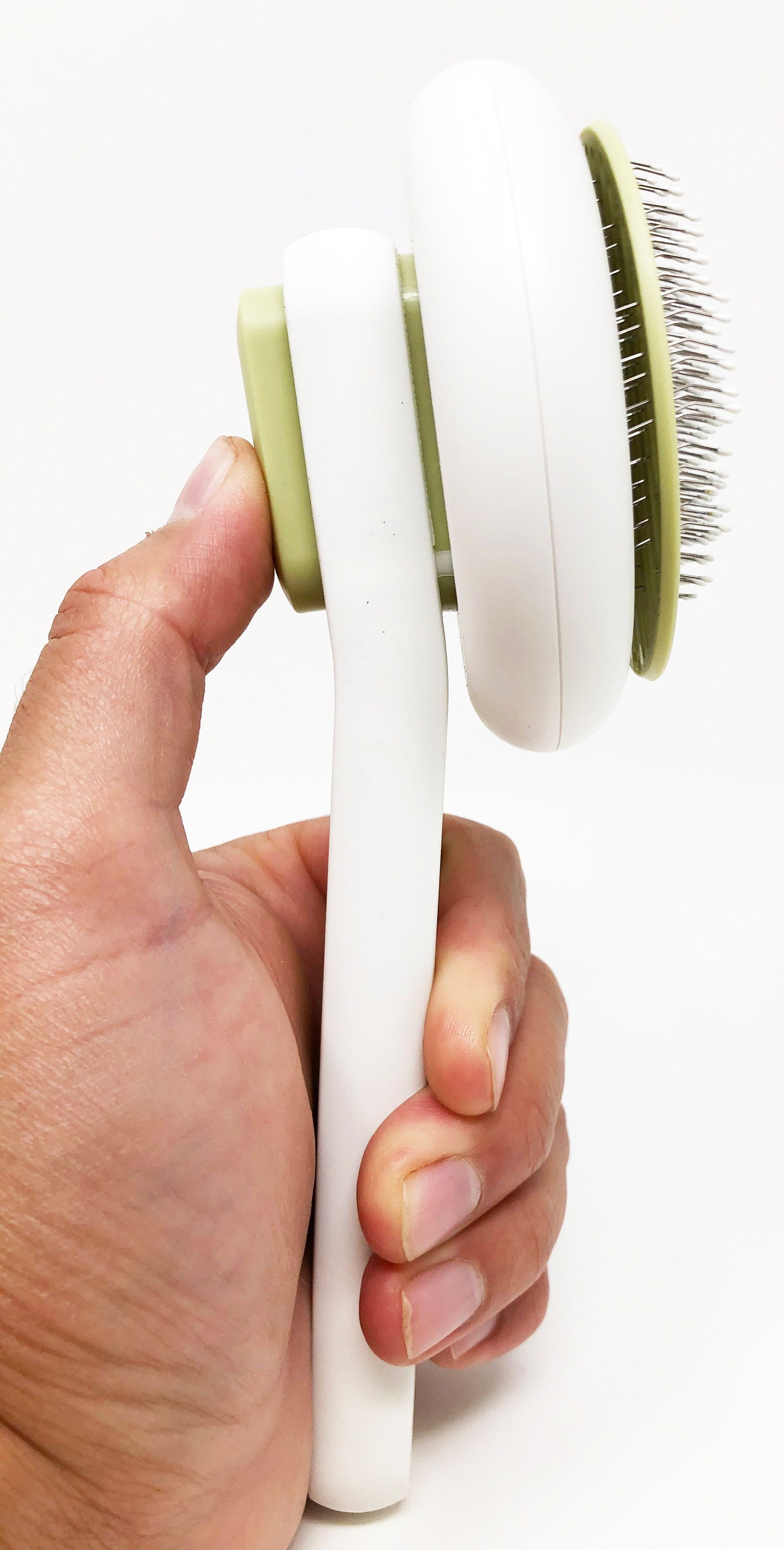 Hand holding a white grooming tool with a green brush head on a white background