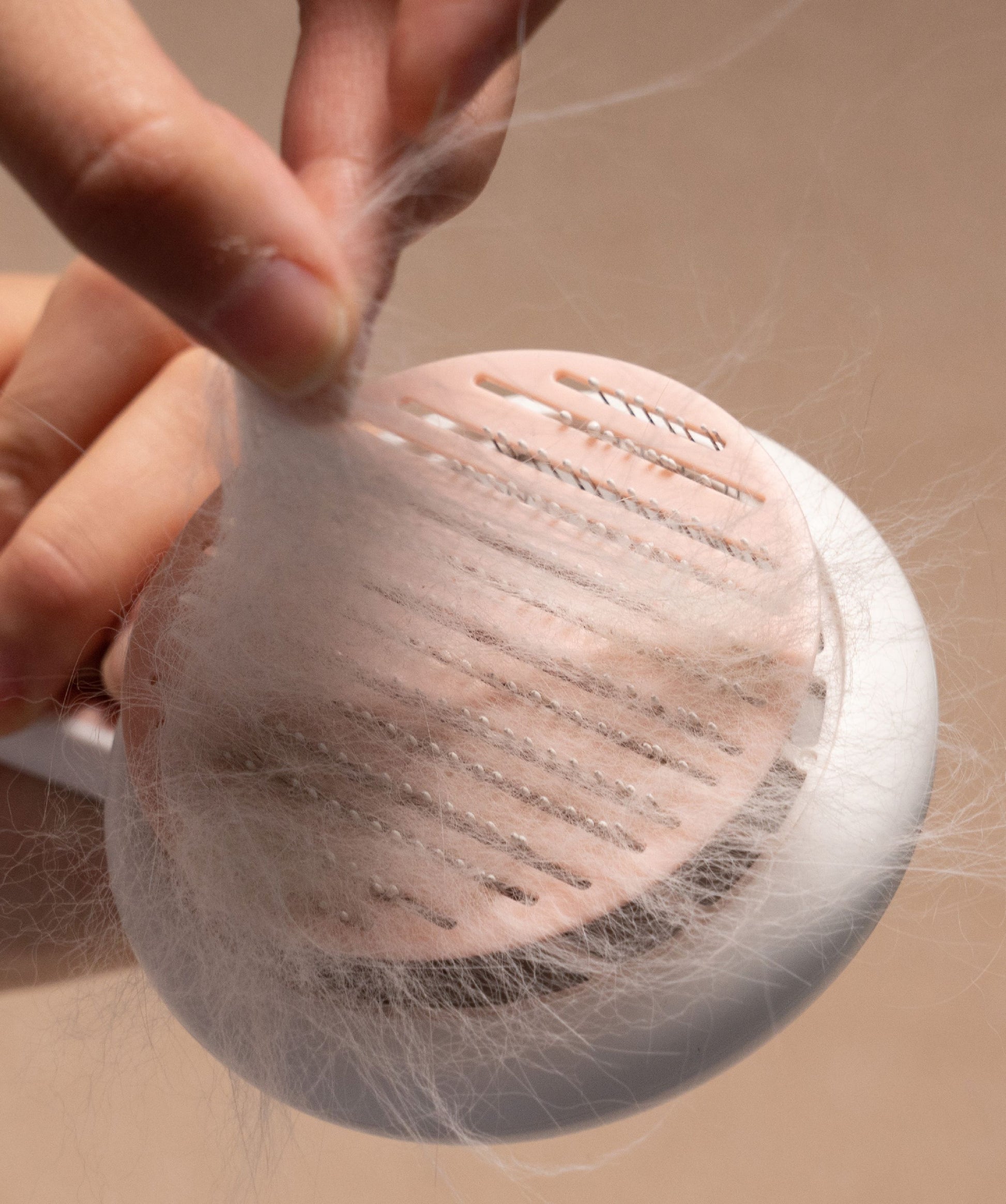 Person holding a hair removal brush with hair collected on it against a beige background