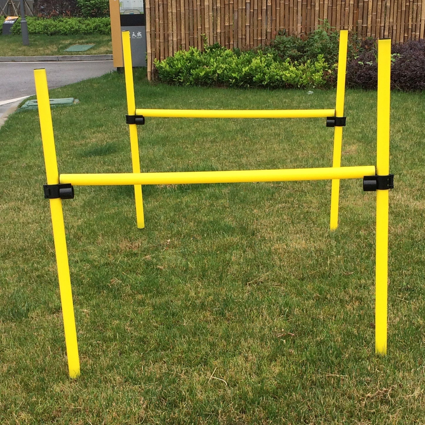 Yellow dog agility hurdle on grass with a wooden fence in the background