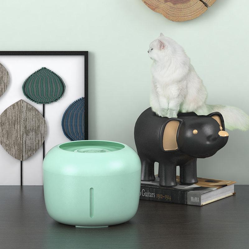 Mint green diffuser on a table with a black elephant figurine and a white cat in the background.