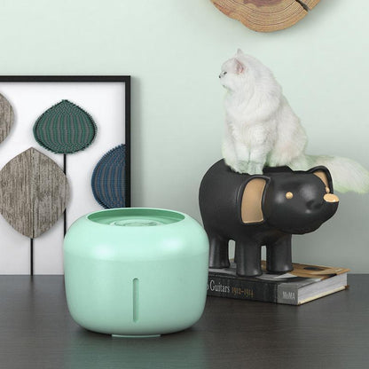 Mint green diffuser on a table with a black elephant figurine and a white cat in the background.