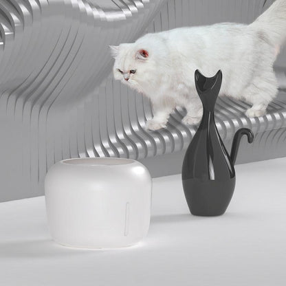 White cat sitting on a modern chair with a black and white cat-shaped vase on a table.