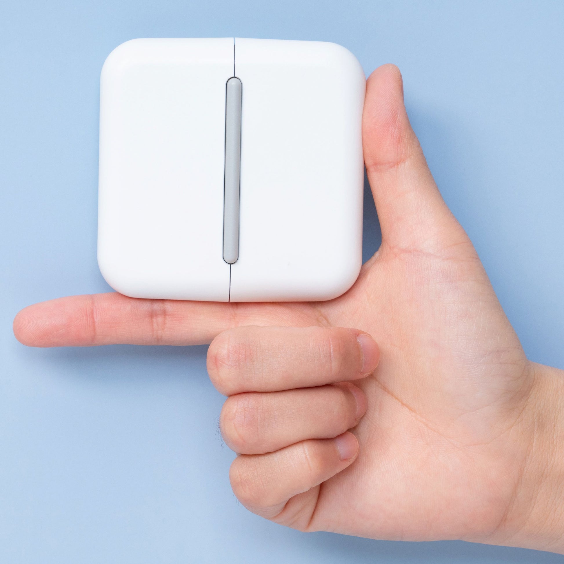 Hand holding a small white device against a light blue background