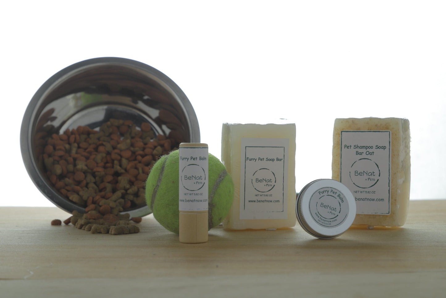 Collection of pet care products including a bowl, balls, and soap bars on a wooden surface.