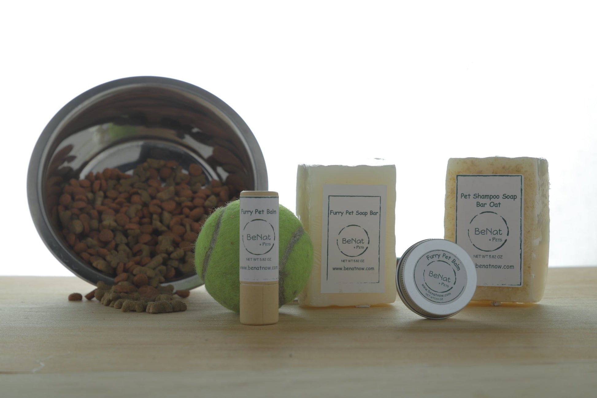 Collection of pet care products including a bowl, balls, and soap bars on a wooden surface.