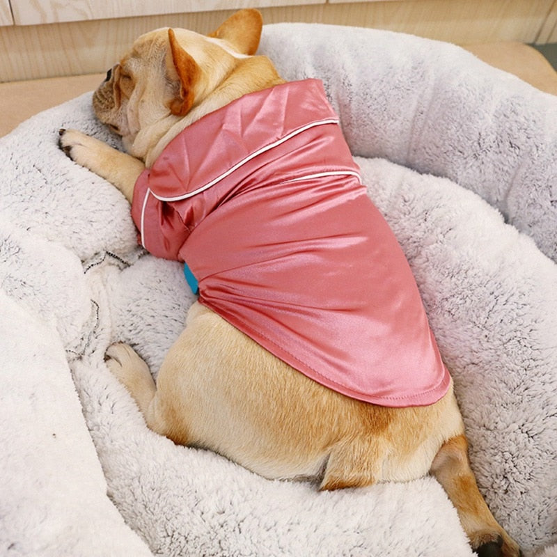 Dog wearing a pink outfit lying on a fluffy white cushion.