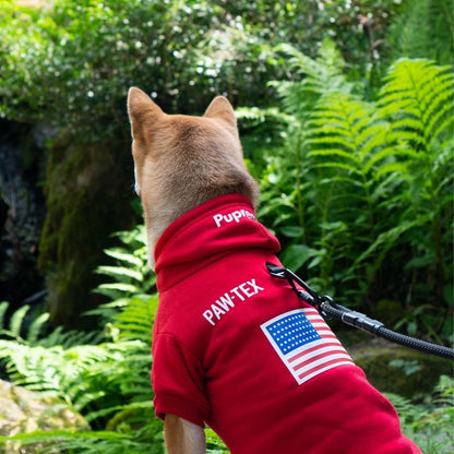 Dog wearing a red PAW-TEX jacket with an American flag patch in a forest setting
