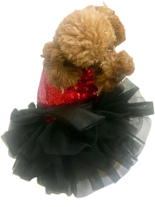 Small dog wearing a red sequin top and black tutu on a white background