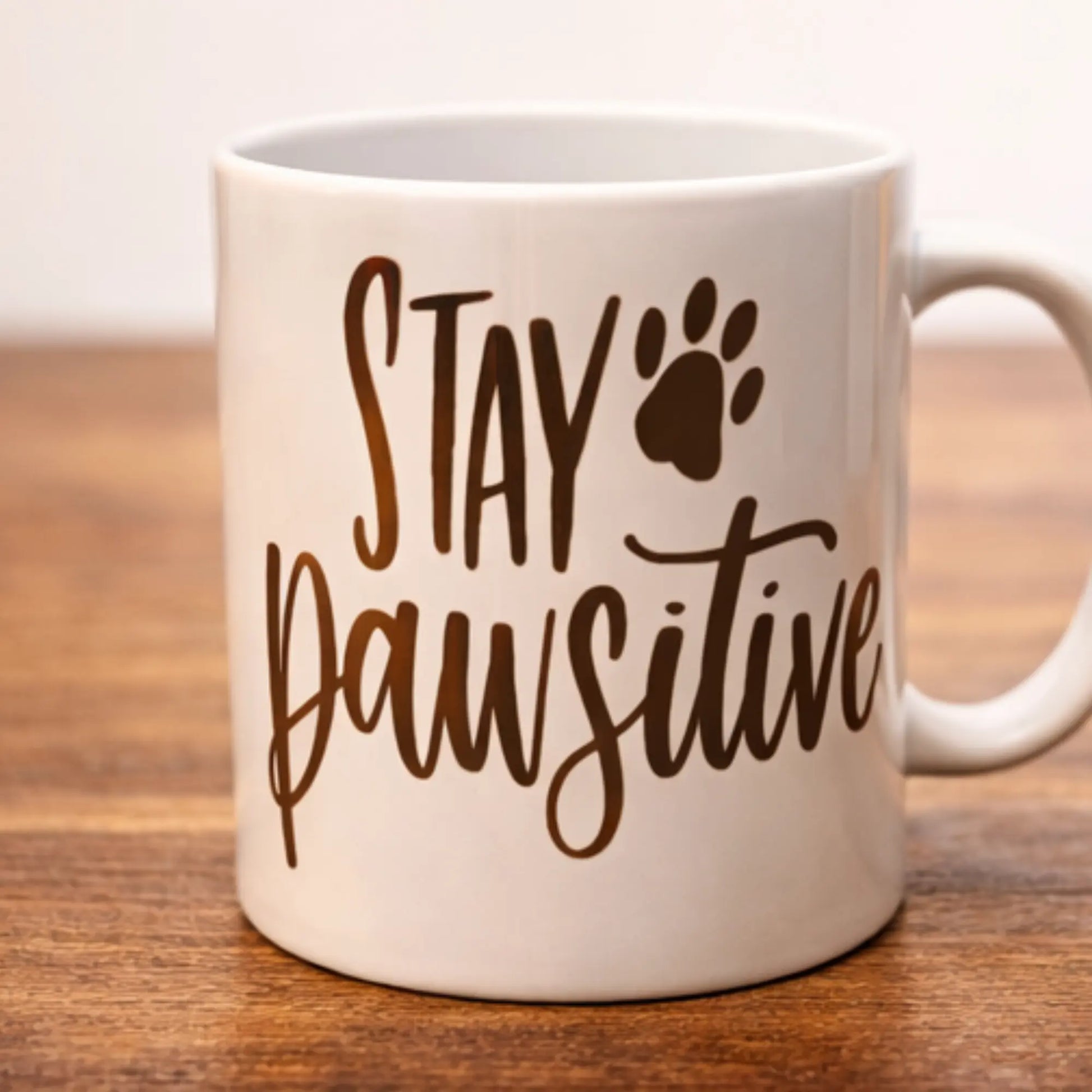 White mug with 'Stay Pawsitive' text on a wooden surface