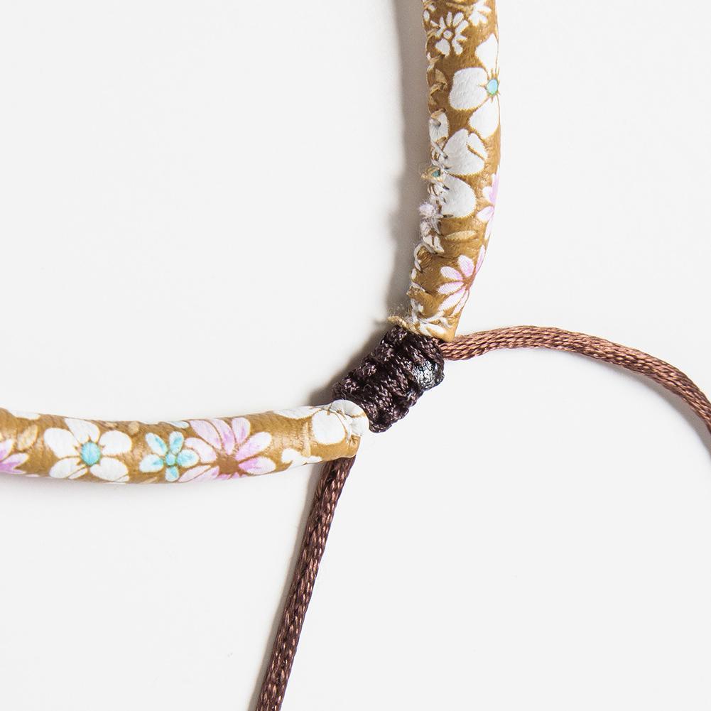 Close-up of a floral-patterned bracelet with a dark brown cord on a white background