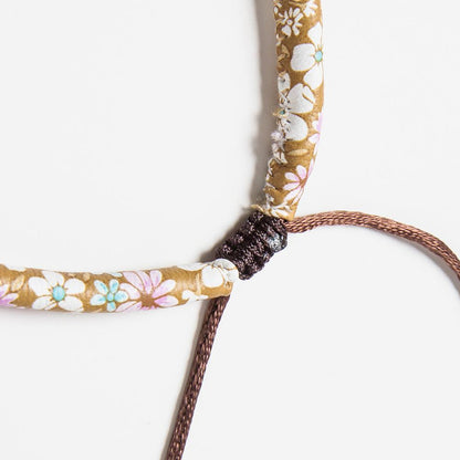 Close-up of a floral-patterned bracelet with a dark brown cord on a white background