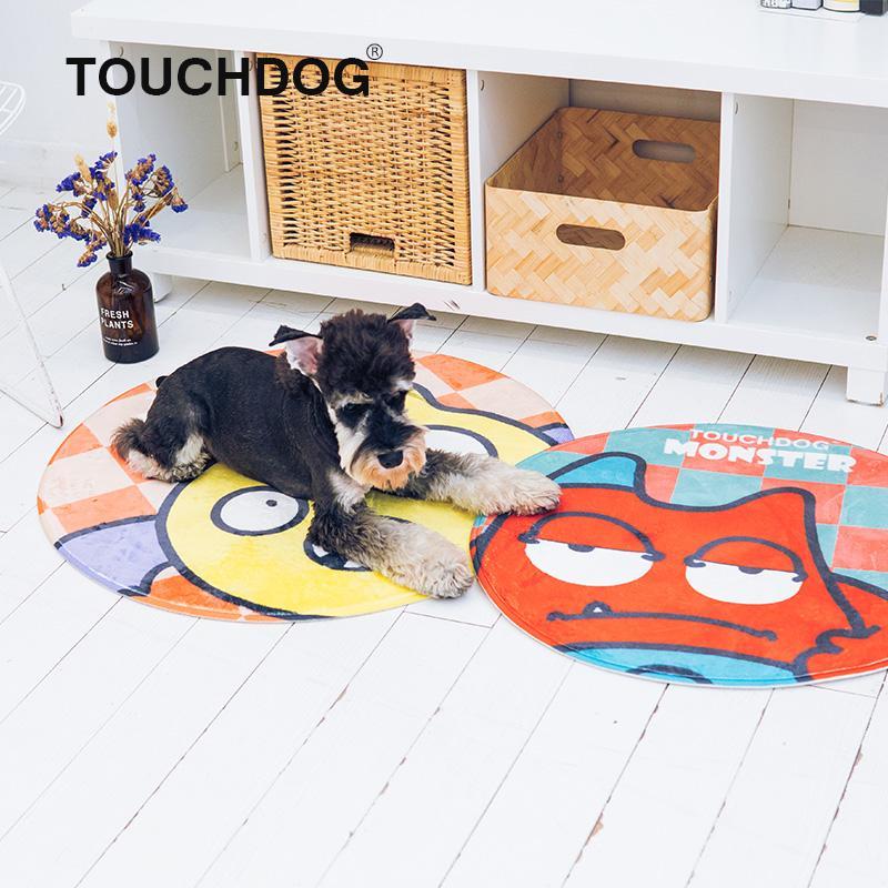 Dog lying on a colorful round mat with 'TOUCHDOG' branding, in front of a white cabinet with wooden baskets.