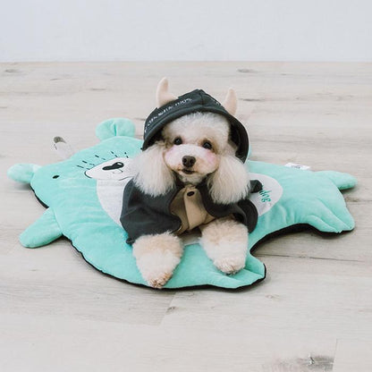 Small dog wearing a black outfit with a hood, sitting on a green star-shaped mat.