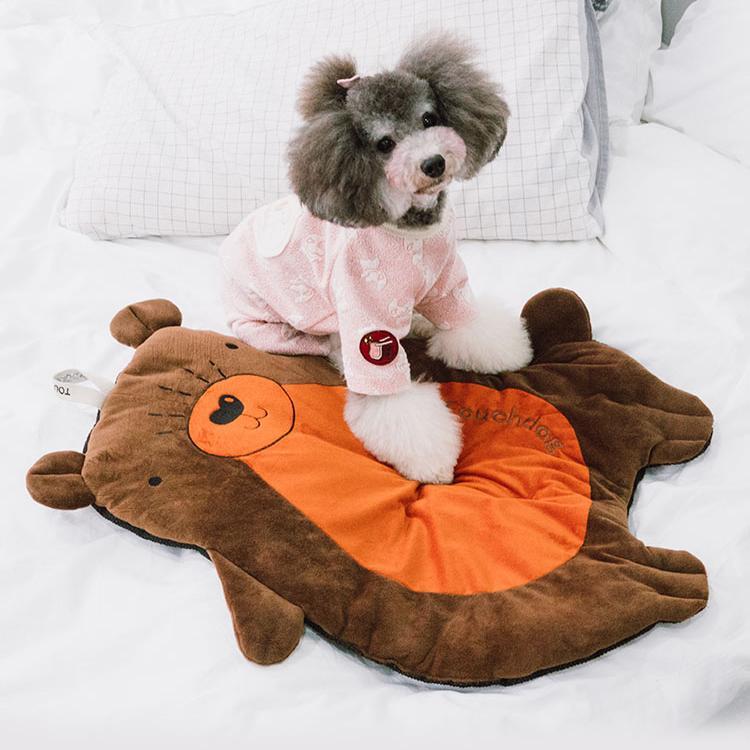 Dog in a pink outfit sitting on a brown and orange bear-shaped mat.
